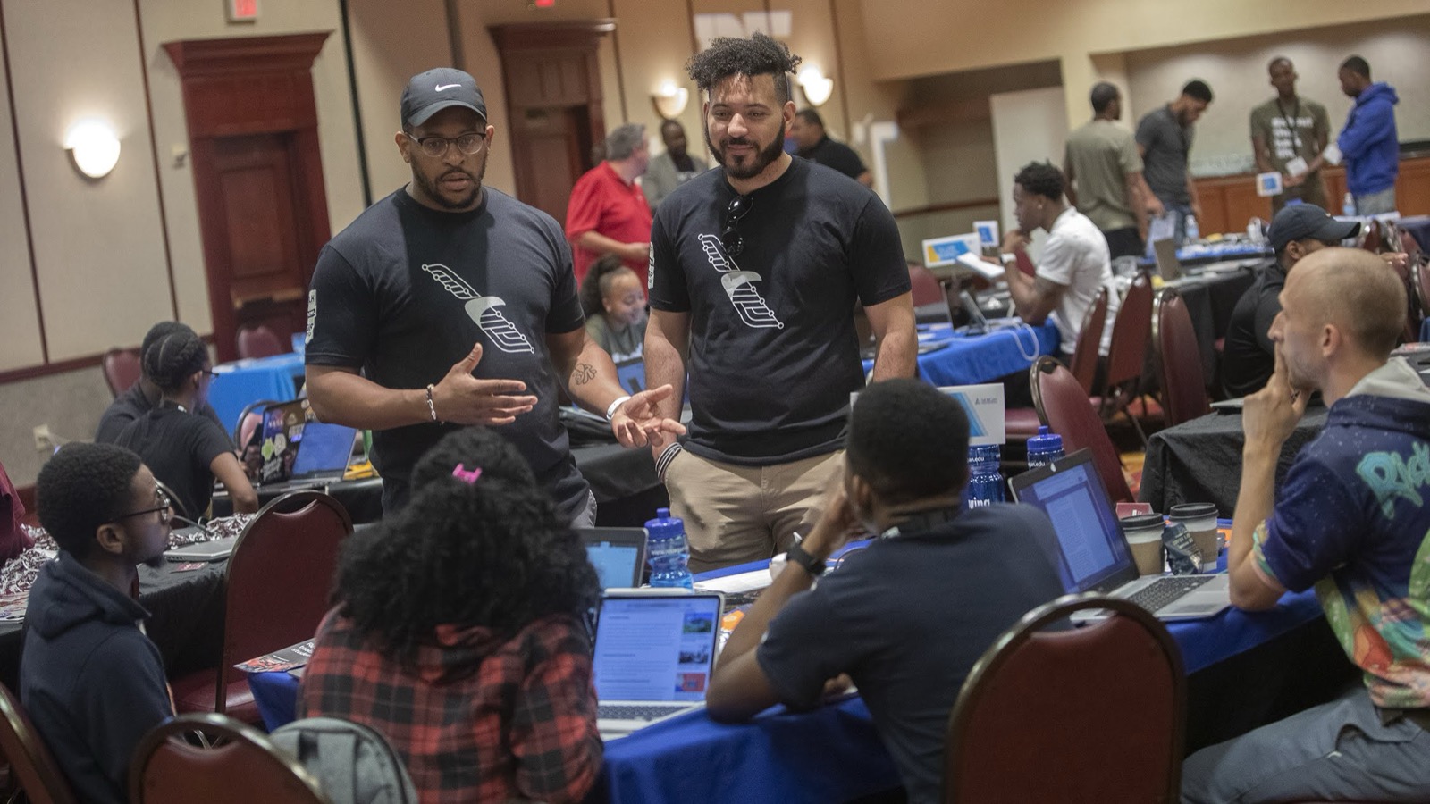 Tre Stewart and a colleague facilitating a hands-on American Airlines workshop with attendees around laptops